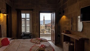 Une chambre d’hôtel avec un lit parsemé de pétales de rose, une vue sur le paysage urbain avec une tour, et un balcon donnant sur la ville.