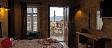 A hotel room with a bed adorned with rose petals, a view of a cityscape with a tower, and a balcony with a view of the city.