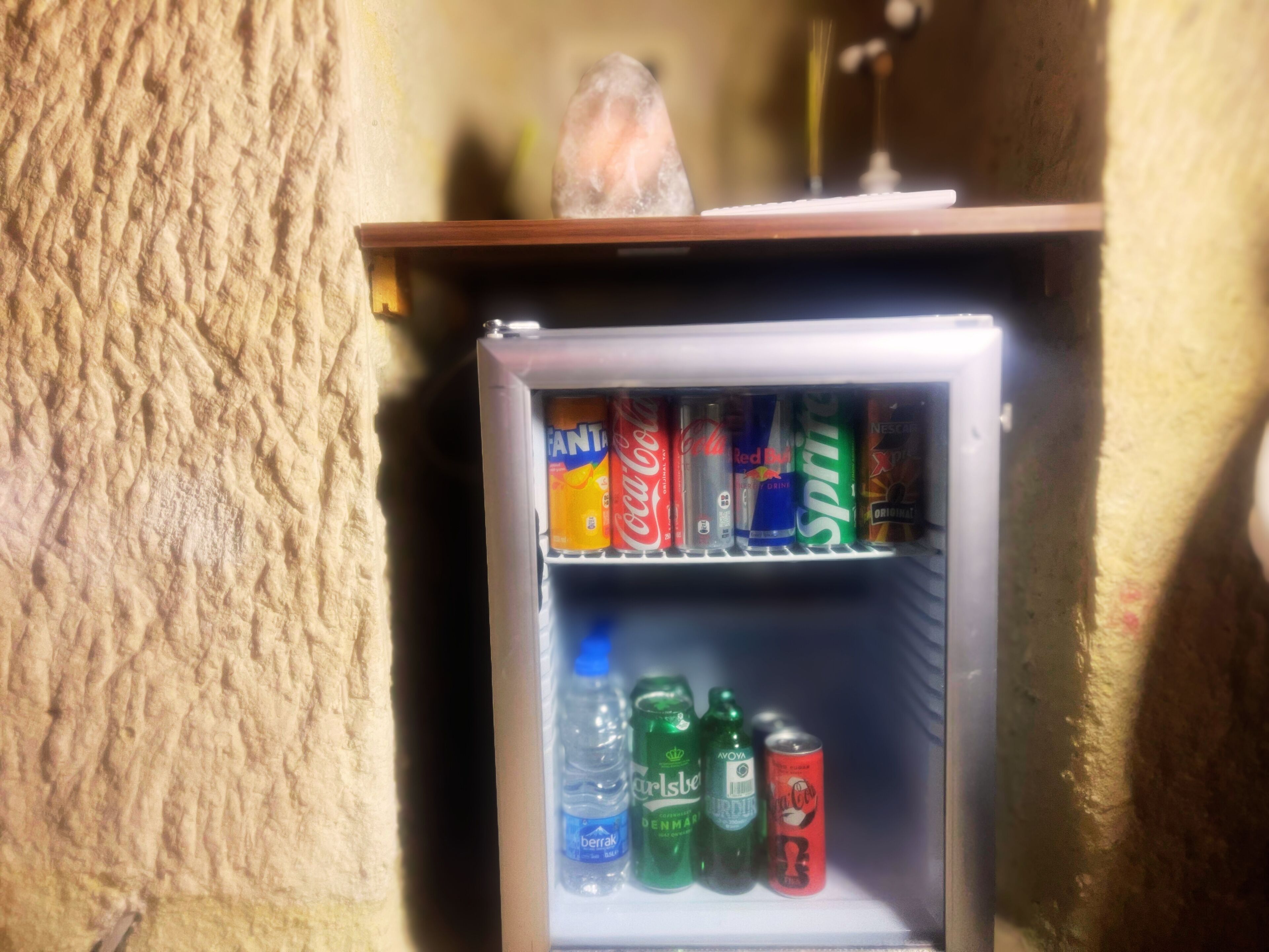 A small refrigerator stocked with various beverages including soda cans and bottled water.