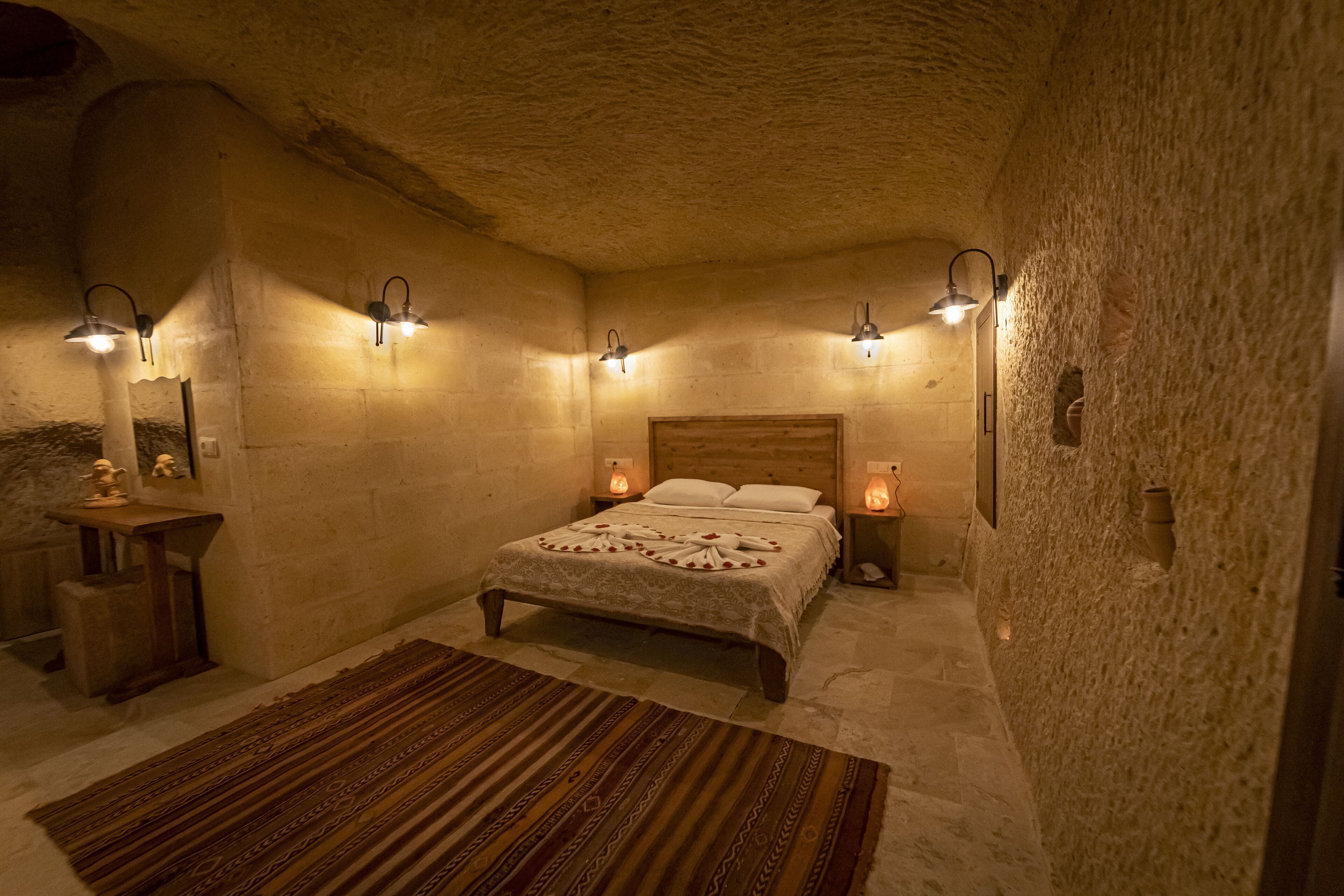 A bedroom with a stone wall, a wooden bed, and four wall-mounted lights.