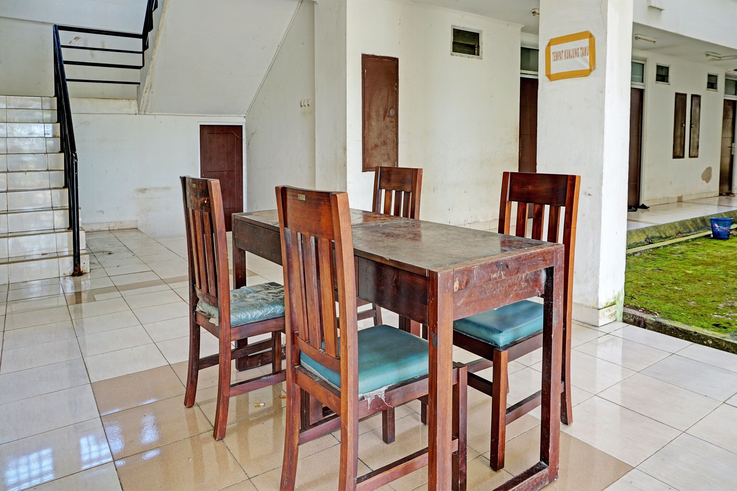 A dining area with a wooden table and chairs, a staircase, and a sign indicating a room number.