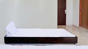 Un lit simple dans une chambre dotée d’une tête de lit en bois, de draps blancs et d’un sol carrelé.