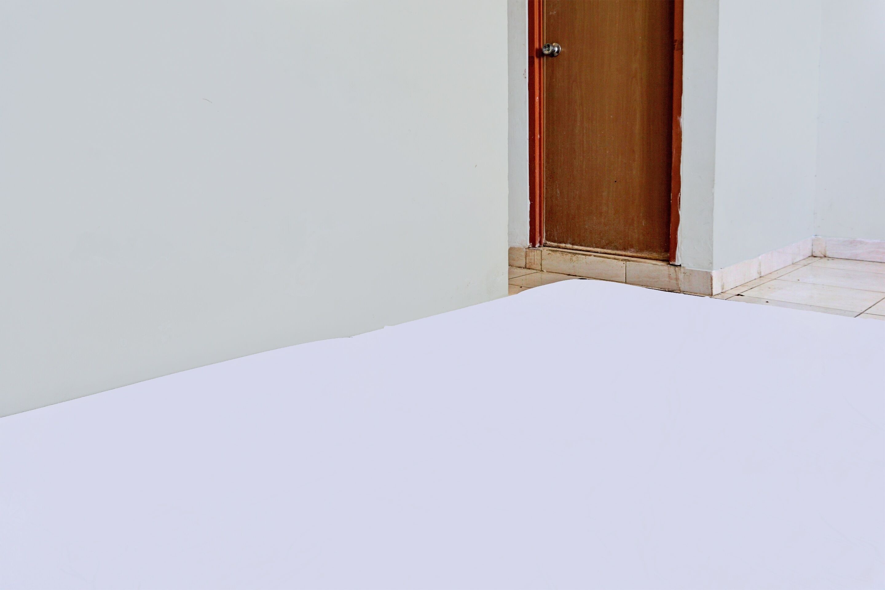 Una habitación blanca con puerta de madera y suelo de baldosas.