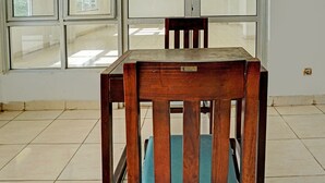 Une table de salle à manger en bois, des chaises, une fenêtre et un sol carrelé.