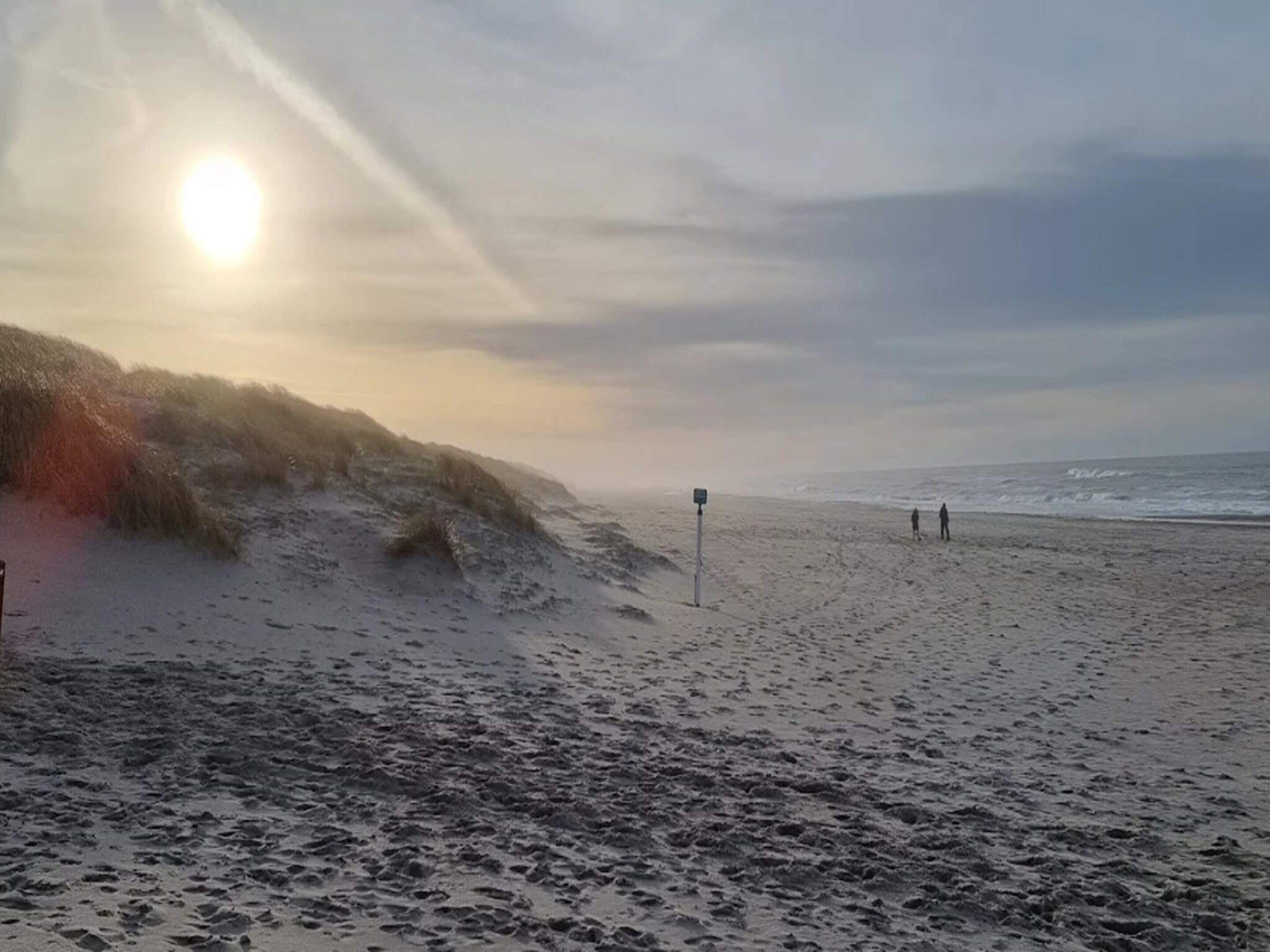 A beach with a sandy shore, waves, and a few people walking.