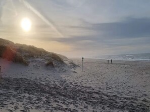 En strand med en sandstrand, vågor och några få personer som promenerar.