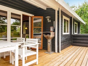 A wooden deck with a white table and chairs, a metal outdoor sink, and a window overlooking greenery. - 6 Person Holiday Home in Henne (Henne)