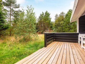 Una terraza de madera con baranda negra, rodeada de follaje y árboles.