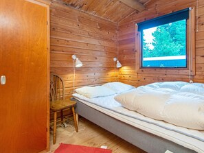 Habitación de cabaña de madera con una cama, dos lámparas fijadas a la pared, un ventanal con vistas a la vegetación y una puerta.