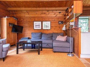 A cozy cabin interior with a sofa, a coffee table, a TV, and a bookshelf. - 6 Person Holiday Home in Henne (Henne)