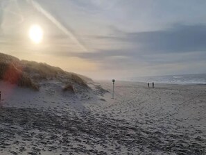 A beach with waves, a clear sky, and a few people walking. - 6 Person Holiday Home in Henne (Henne)