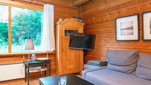 A cozy cabin interior with a wooden interior, a television mounted on a cabinet, a sofa, and a table with remote controls. - 6 Person Holiday Home in Henne (Henne)