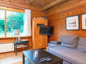 A cozy cabin interior with a wooden interior, a television mounted on a cabinet, a sofa, and a table with remote controls. - 6 Person Holiday Home in Henne (Henne)