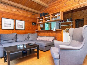 Una sala de estar acogedora con un sofá gris, un sillón a juego y una mesita de centro. Encima del sofá hay estanterías con varios objetos.