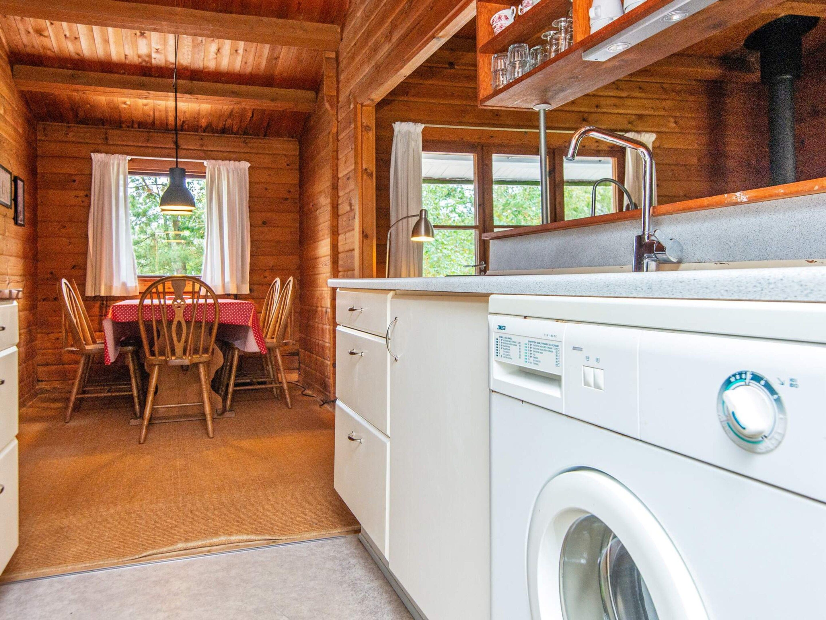 Una cocina funcional con lavadora, una mesa de comedor con sillas y una ventana con cortinas.