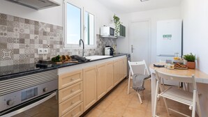 A modern kitchen with patterned tiles, a built-in oven, a sink, and a dining area with a chair and table. - HARMONIA Apartment with Spectacular Ocean View (Portocolom)