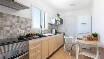 A modern kitchen with patterned tiles, a built-in oven, a sink, and a dining area with a chair and table.