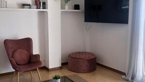 A living room with a red chair, a glass coffee table, a round ottoman, a potted plant, and a flat-screen TV mounted on the wall. - HARMONIA Apartment with Spectacular Ocean View (Portocolom)