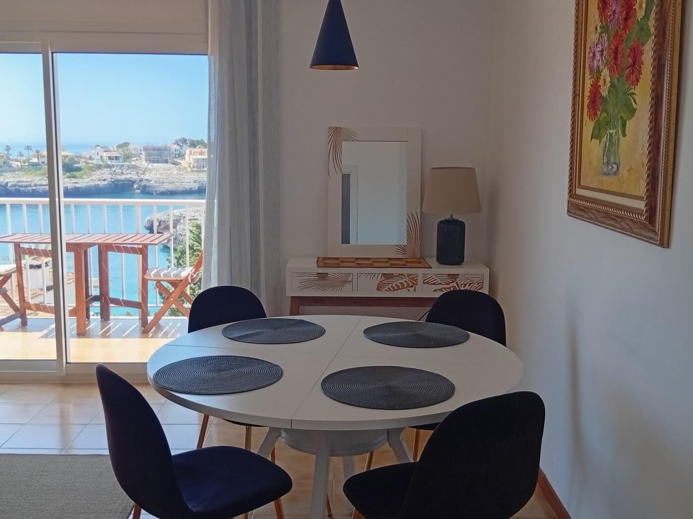 Un comedor con una mesa redonda, sillas negras, una lámpara colgante azul, un espejo decorativo y un cuadro.