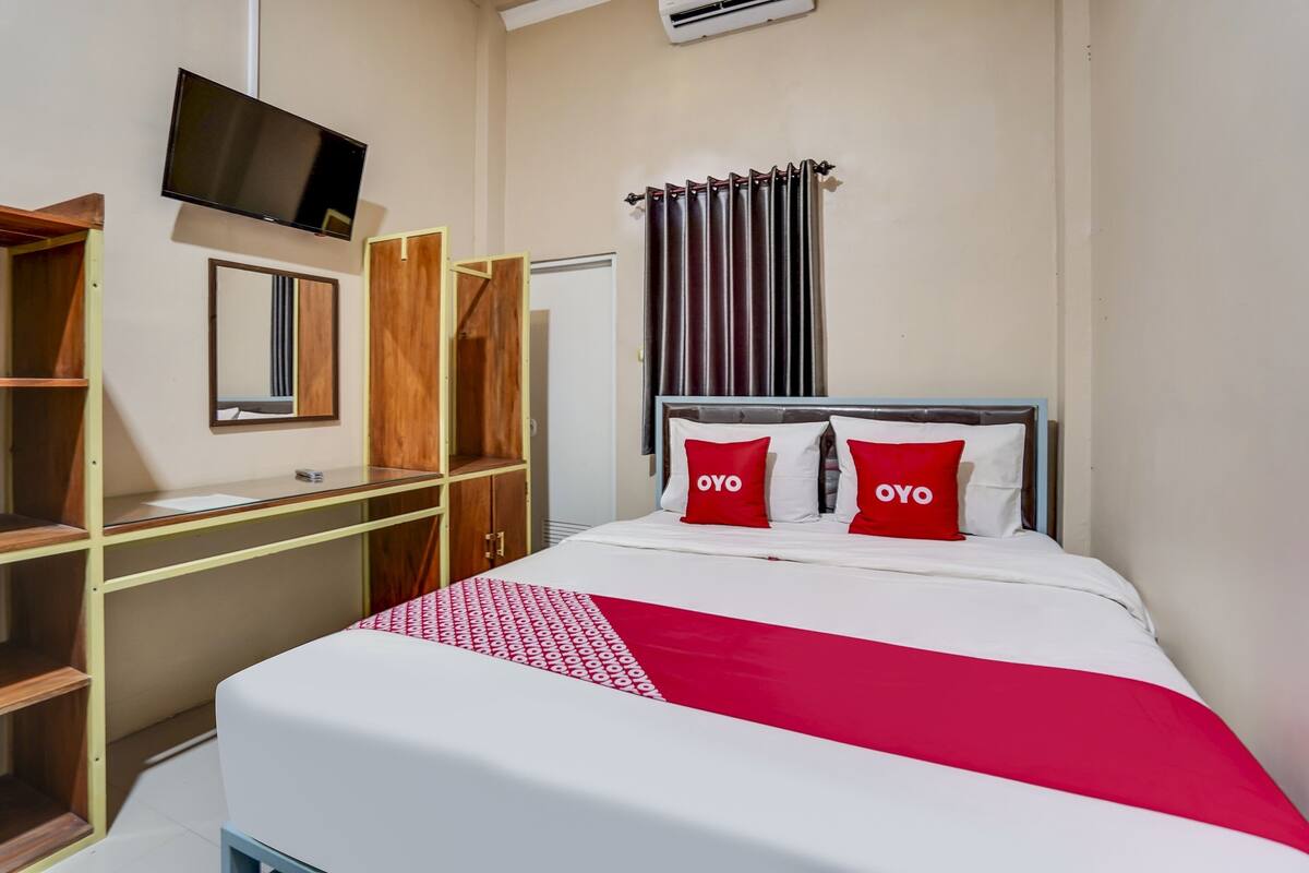 A hotel room with a bed, a TV mounted on the wall, a wardrobe, and a window with curtains.