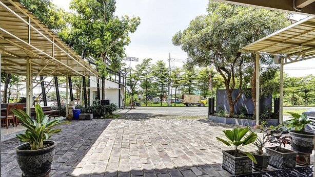 A covered outdoor area with a paved walkway, potted plants, and a seating area with tables and chairs. - OYO Flagship 90886 Sunset View Homestay (Mojokerto)