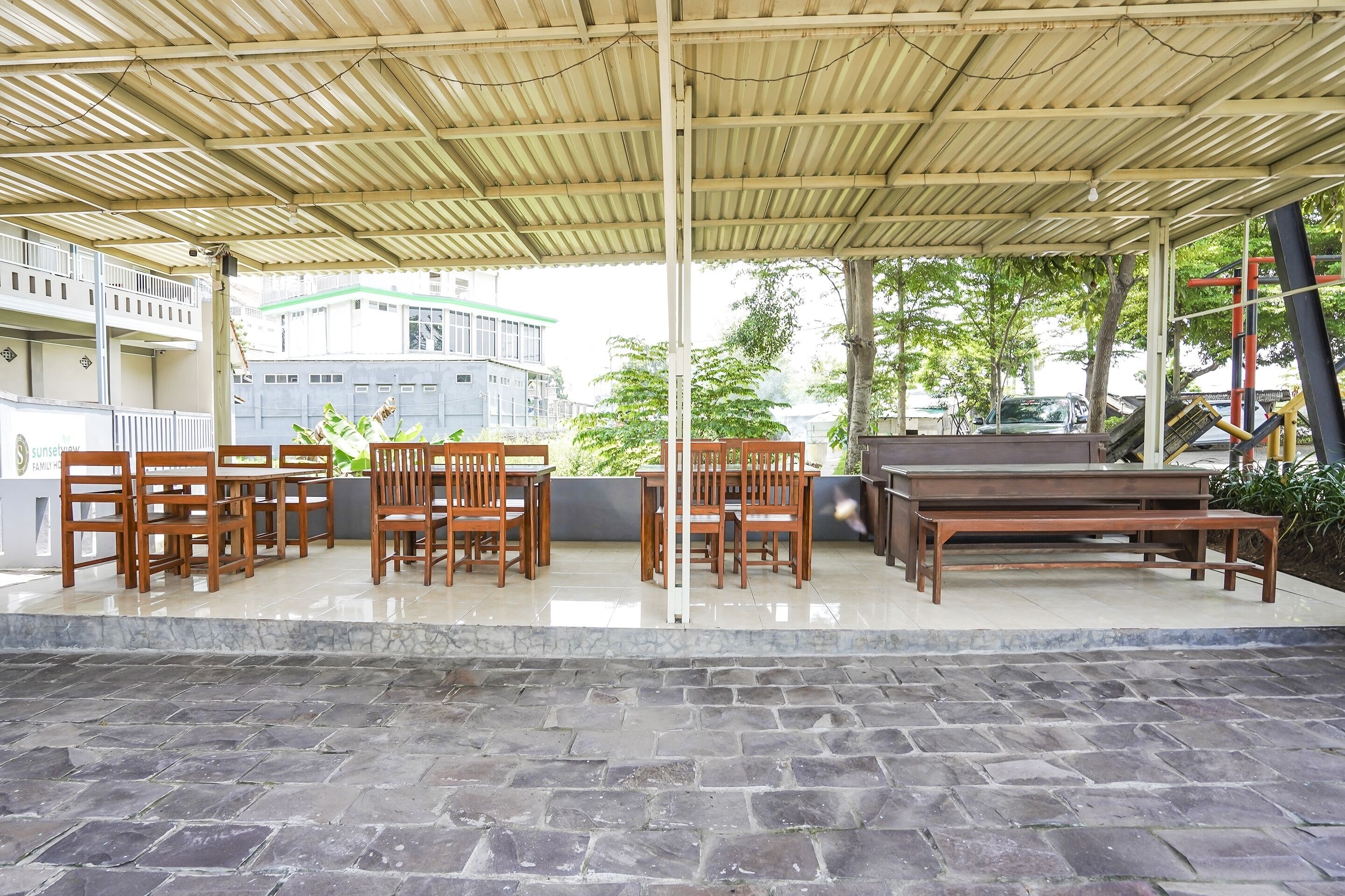 An outdoor patio with wooden tables and chairs, a barbecue grill, and a stone-tiled floor.