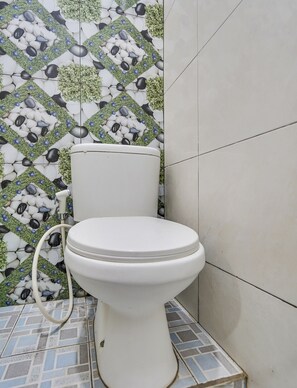 A toilet with a white seat and lid, positioned on a tiled floor with a geometric pattern. - OYO Flagship 90886 Sunset View Homestay (Mojokerto)