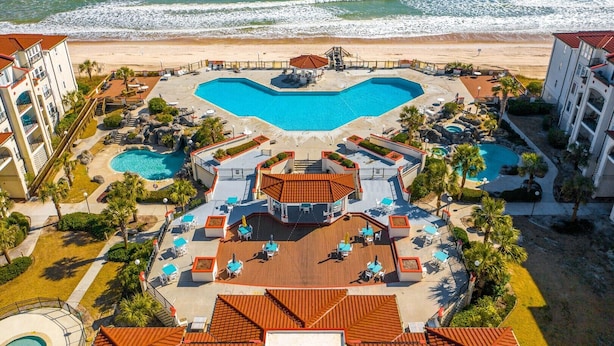 Een resort met een groot centraal zwembad, een kleiner zwembad en een strandgedeelte.