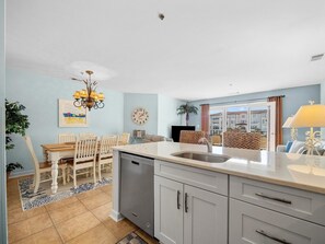 A modern kitchen with grey cabinets, a central island, and a dining area with a wooden table and chairs.