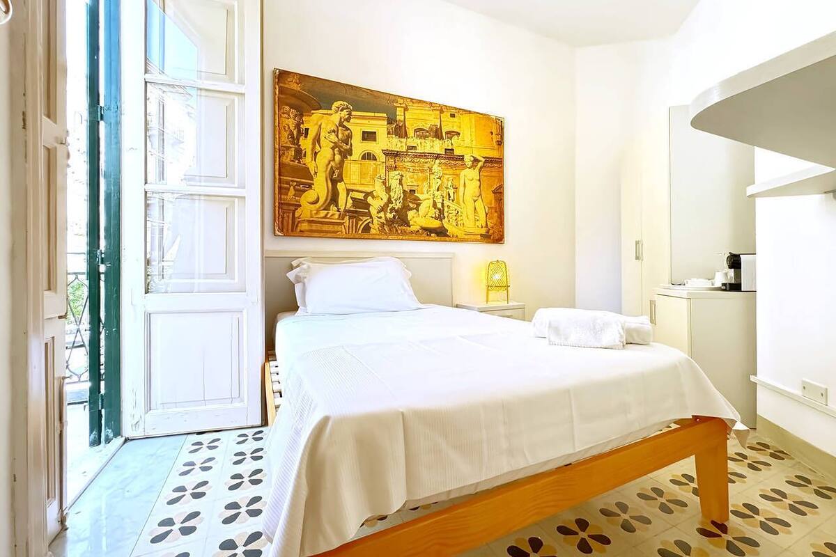A bedroom with a bed, a painting, a nightstand, and a lamp.