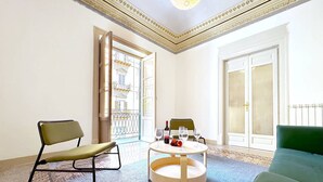 A room with a green sofa, a black and green chair, a round wooden table with two wine glasses and a bottle, and a view of a building through an open door. - Solemar Sicilia - Monacò Rooms (Palermo)
