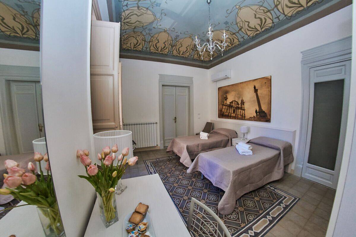 A hotel room with two beds, a chandelier, a painting of the Eiffel Tower, and a vase of tulips.
