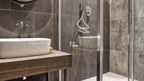 A modern bathroom with a glass-enclosed shower, a round mirror, and a wooden vanity. - Hotel Vitruvio (Milan)