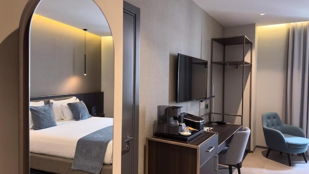 A modern hotel room with a bed, a desk with a coffee maker, a TV, and a chair. - Hotel Vitruvio (Milan)