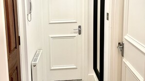 Un pasillo con una puerta blanca, un radiador, una lámpara colgante y un espejo negro en la pared.
