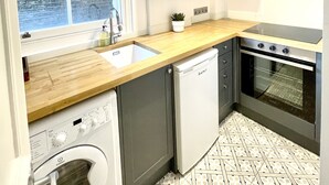 Cocina compacta con lavavajillas integrado, horno y ventana con vista a un muro de ladrillo.