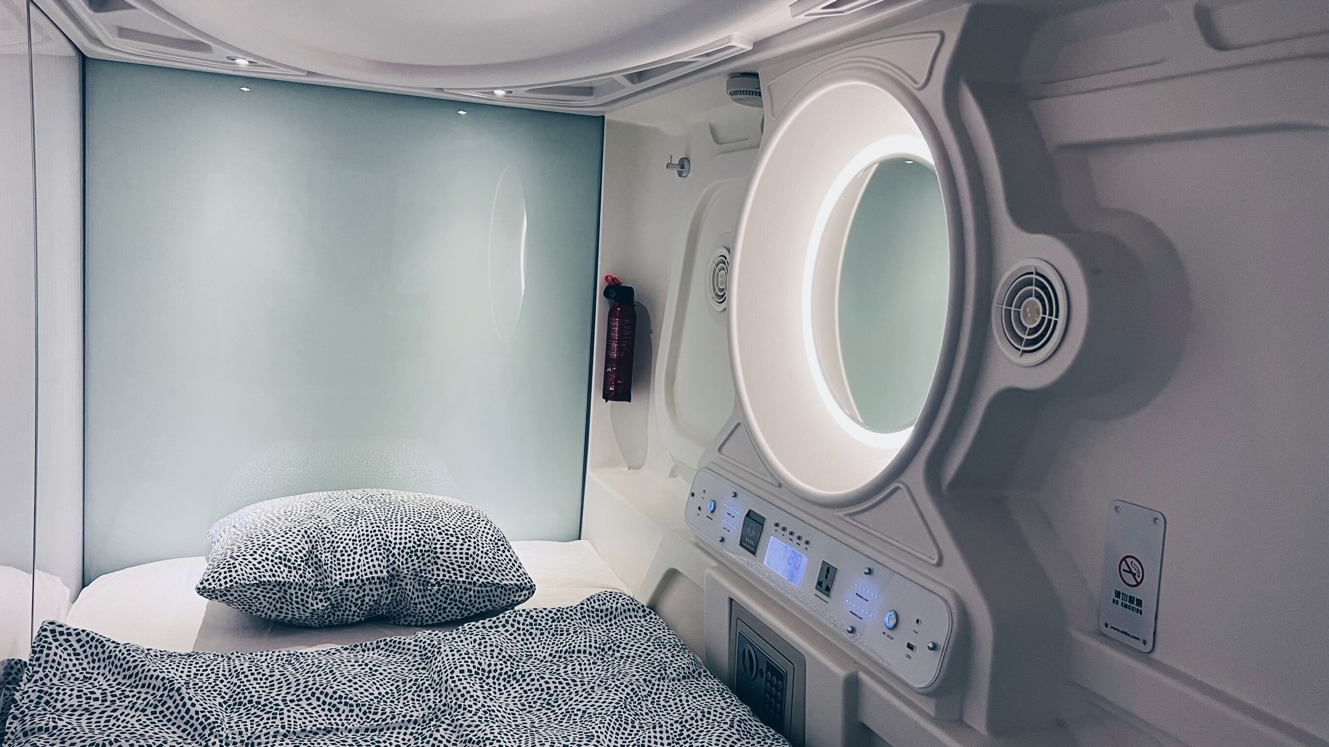 A modern bathroom with a large mirror, a control panel, and a bed with patterned bedding.