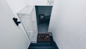 A stairwell with a white wall, a metal handrail, a door with a 'HELLO' mat, and a 'SNOKI' sign on the wall.