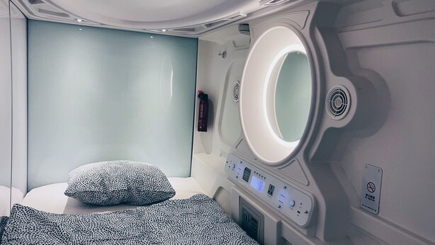 A modern bathroom with a large mirror, a control panel, and a bed with patterned bedding.