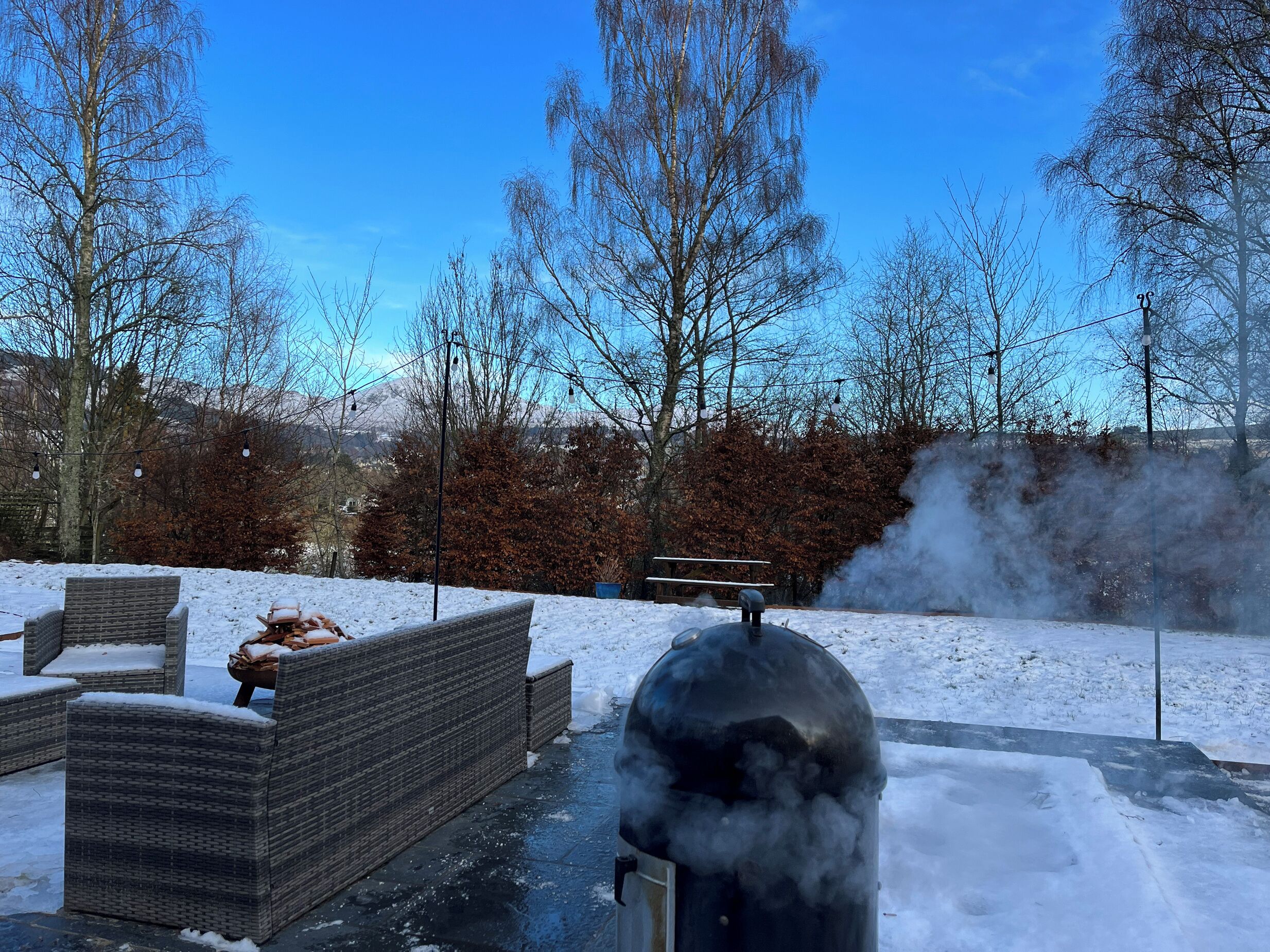 A patio area with wicker furniture and a barbecue grill emitting smoke.