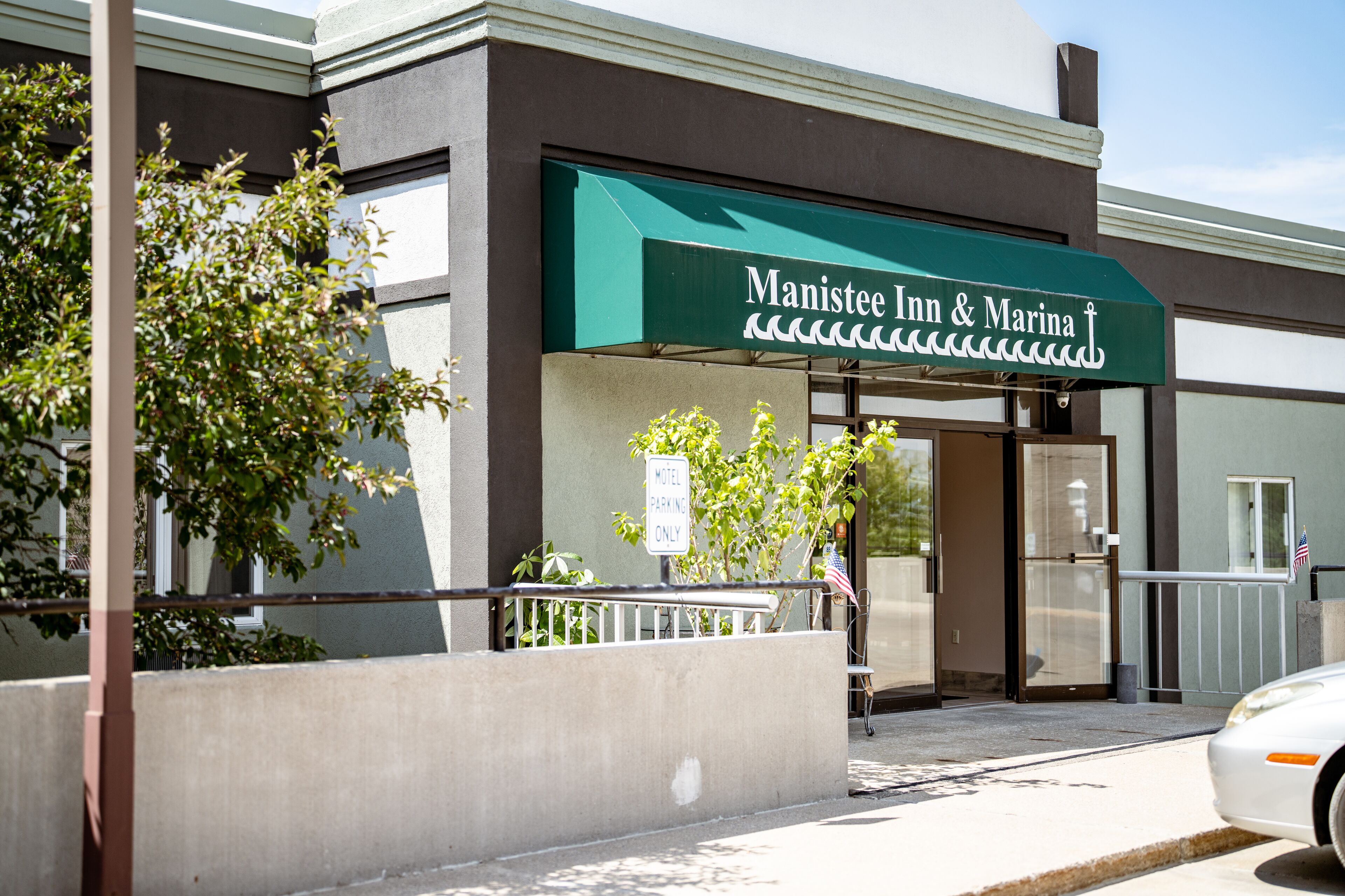 The exterior of Manistee Inn & Marina with a green awning, a sign indicating 'Motel Parking Only', and a flag outside the entrance.