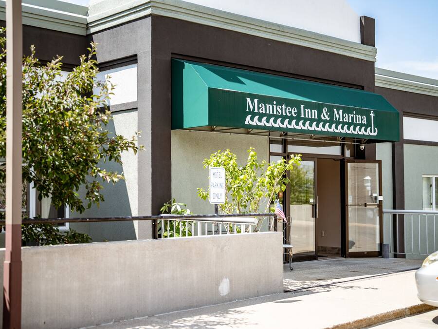The exterior of Manistee Inn & Marina with a green awning, a sign indicating 'Motel Parking Only', and a flag outside the entrance.