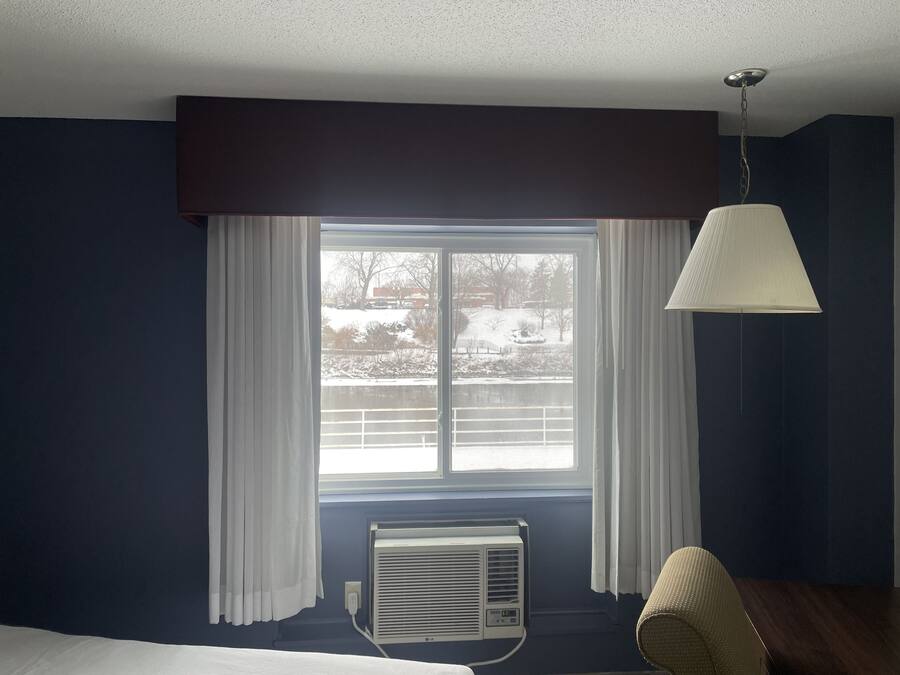 A hotel room with a large window, white curtains, a ceiling fan, and an air conditioning unit.