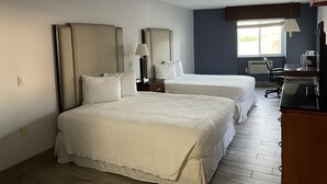 A hotel room with two beds, a desk, a chair, a lamp, and a window.