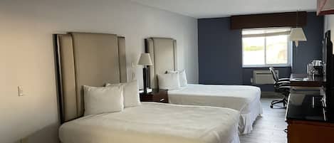 A hotel room with two beds, a desk, a chair, a lamp, and a window.