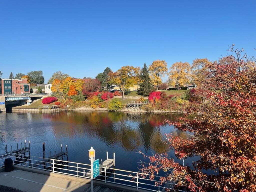 A riverside view with a bridge, autumn foliage, and a dock with a lamp post.