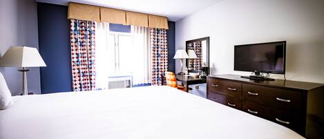 A hotel room with a large bed, two bedside tables with lamps, a dresser, a television, and patterned curtains.
