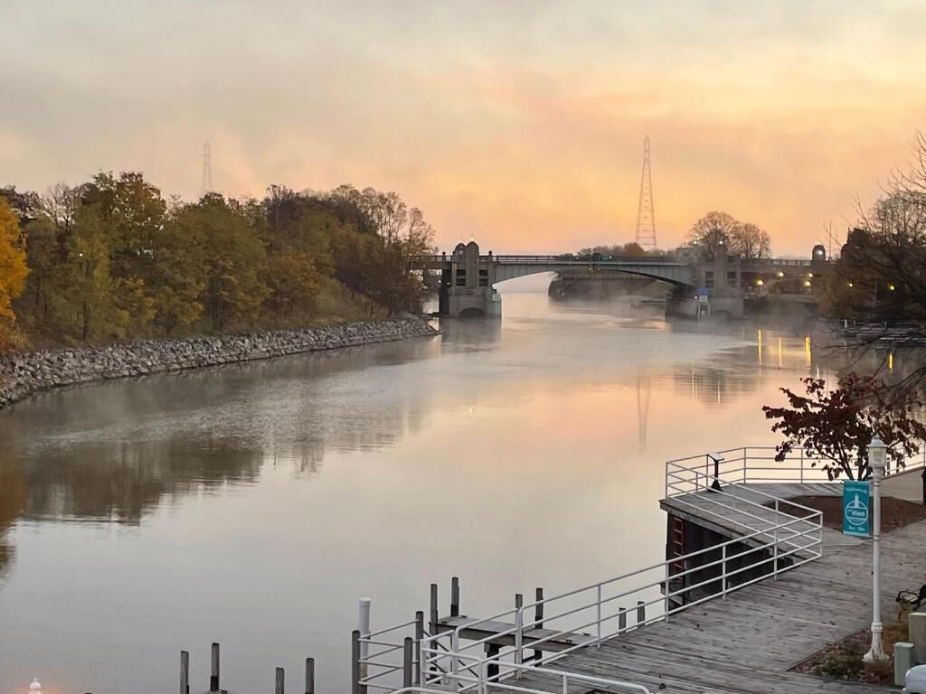 Ein ruhiger Fluss mit einer Brücke, einem hölzernen Steg und einem Fußweg.