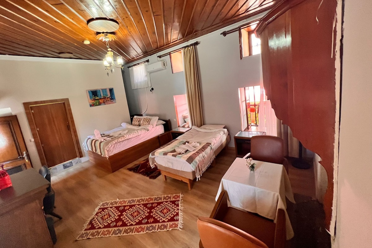 Ein Zimmer mit zwei Betten, einer Holzbalkendecke, einem Esstisch und einem kleinen Tisch mit einer Vase.