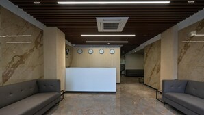 Uma área de recepção com pisos de mármore, dois sofás, um balcão de recepção e um teto com ripas de madeira e iluminação embutida.